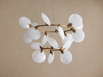 Lyla Chandelier: Modern gold brass chandelier with multiple illuminated circular hand-blown white glass shades, against a plain wall.