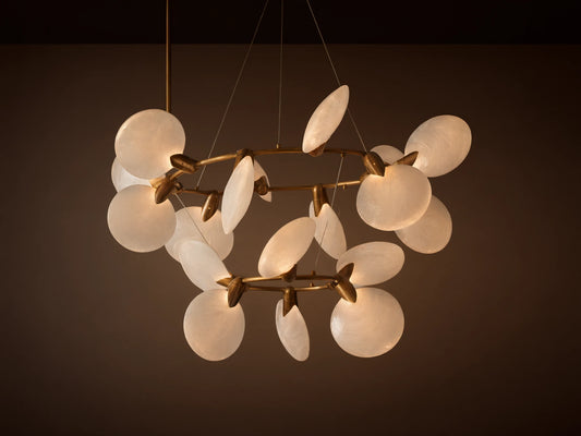 Lyla Chandelier: Modern gold brass chandelier with multiple illuminated circular hand-blown white glass shades, against a plain wall.