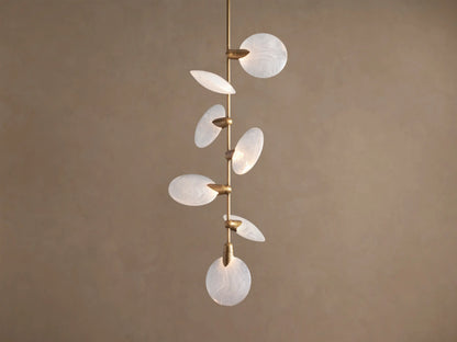 Lyla Pendant: 7 round, swirled hand-blown glass shades with glowing LED lights on a vertical brass stem against a brown wall.