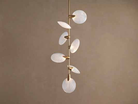 Lyla Pendant: 7 round, swirled hand-blown glass shades with glowing LED lights on a vertical brass stem against a brown wall.