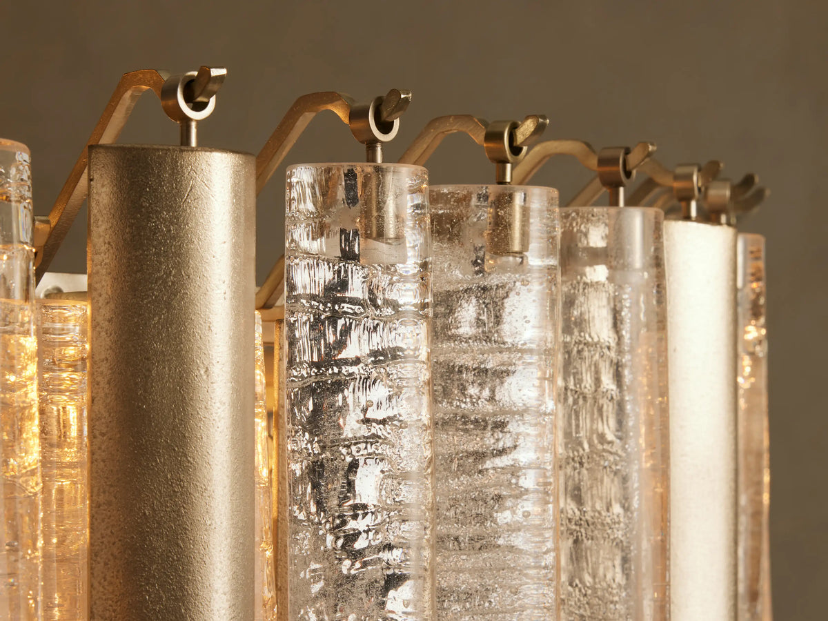 Close-up of Neve Round Chandelier showing champagne aluminum & clear textured glass cylinders glowing, suspended from brass frame.
