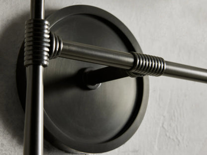 Rhodes Double Sconce with a round, bronze-finished steel backplate and detailed rod design on a textured wall surface.
