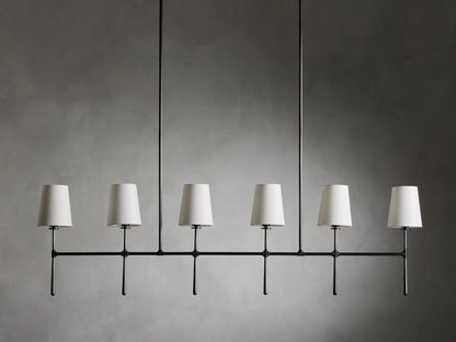 Rhodes Linear Chandelier with six tapered linen shades on a bronze-plated steel frame, suspended against a neutral wall.