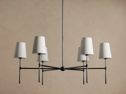 Rhodes Round Chandelier, dark metal frame with six lit tapered linen shades, centered against a warm brown wall.