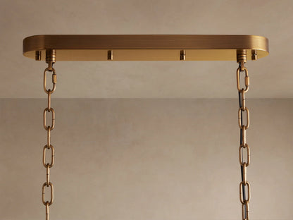 Neve Linear Chandelier. Close-up of an oval brass ceiling plate with two brass chains hanging down against a light-colored ceiling.