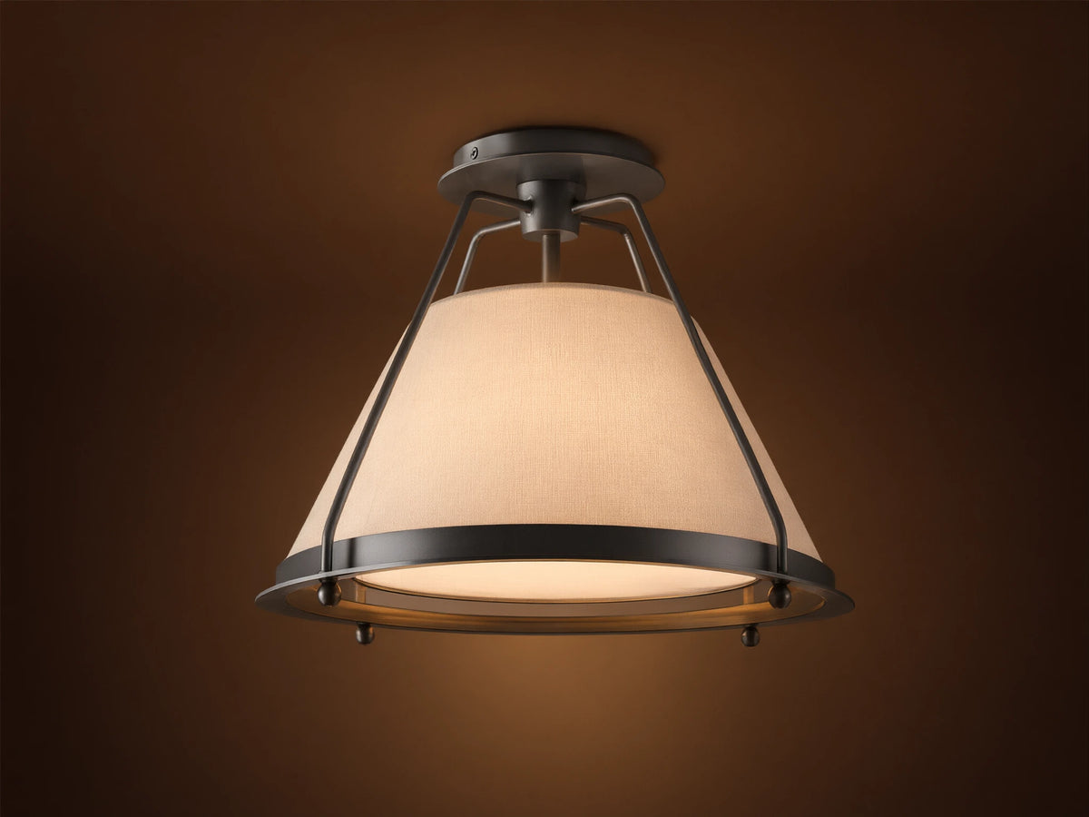 Shelton Flush Mount ceiling light with dark metal frame and large, tapered cream linen shade glowing warmly, mounted on a beige ceiling.