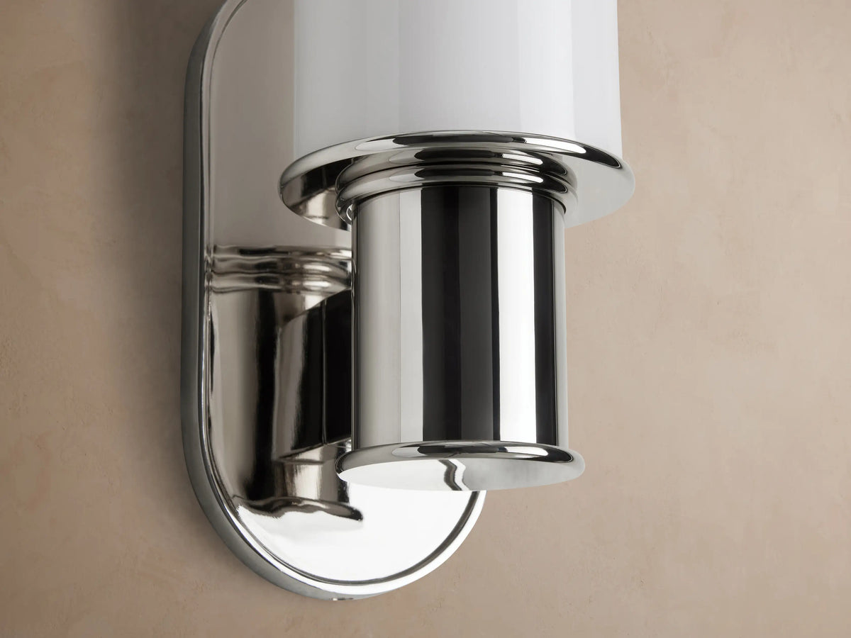 Harlin Sconce with cylindrical milk glass diffuser and polished nickel finish, mounted vertically on a light tan wall.