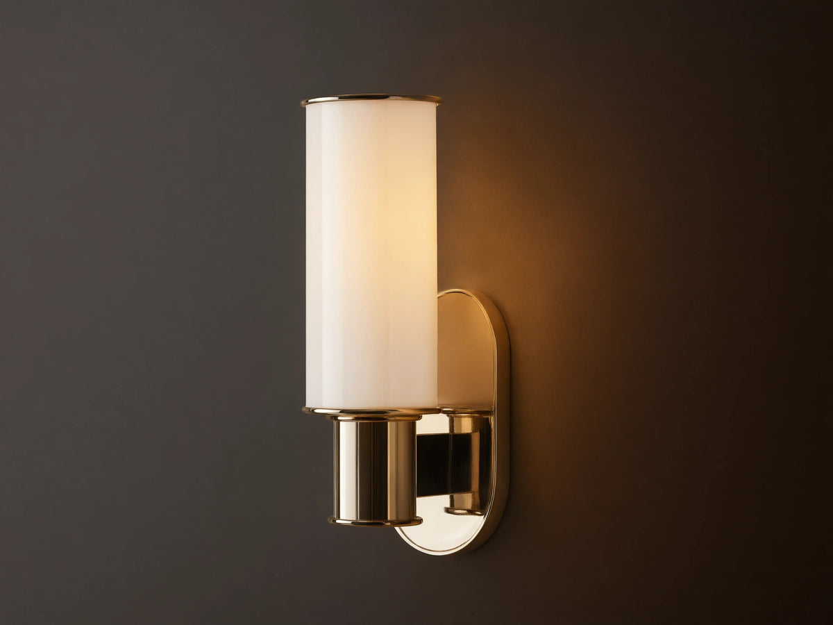 Harlin Sconce in Milk. Polished nickel wall sconce with a lit, vertically oriented milk glass cylinder on a beige wall.