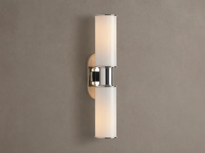 Harlin Double Sconce with two glowing vertical milk glass shades and polished nickel accents, mounted on a textured brown wall.