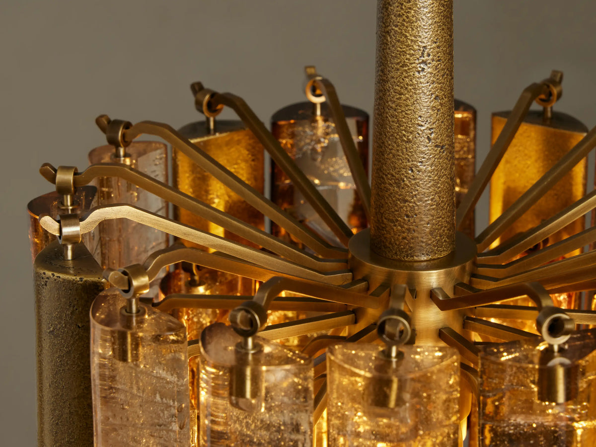 Close-up of Neve Pendant, showing multiple amber/bronze cast glass tubes glowing warmly, some textured, against a dark background.