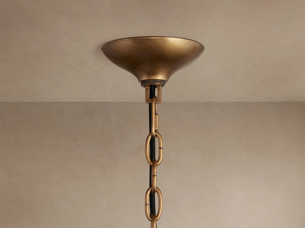 Close-up of Neve Pendant: textured brass central column with radiating arms holding illuminated, textured bronze cast glass elements.