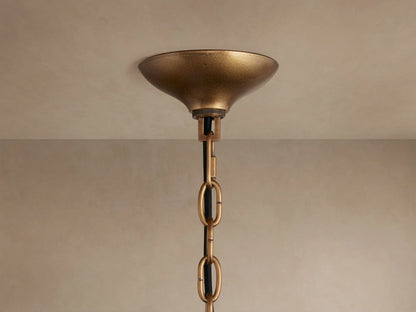 Close-up of Neve Pendant: textured brass central column with radiating arms holding illuminated, textured bronze cast glass elements.