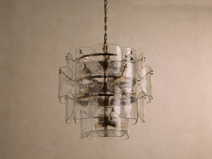 Blaire Round Chandelier with layered, curved clear glass panels creating a textured effect. Lit with warm light, hung by a brass-finished chain.