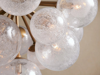 Mandoza Chandelier: Clear and frosted hand-blown glass globes on burnished brass arms, suspended against a light tan background.