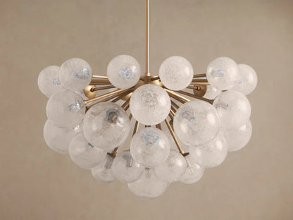 Mandoza Chandelier with a gold-toned frame and many illuminated, textured glass globes against a light brown wall.