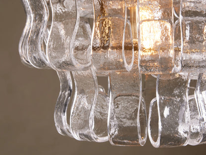 Curved glass strands of the Ghiaccio Pendant form a textured, wavy design around the warm glow of a bulb, mounted on a steel frame.