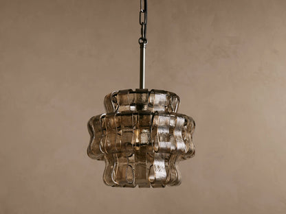 Ghiaccio Pendant with wavy curved glass panels illuminated from within, hanging on a black steel chain against a brown backdrop.