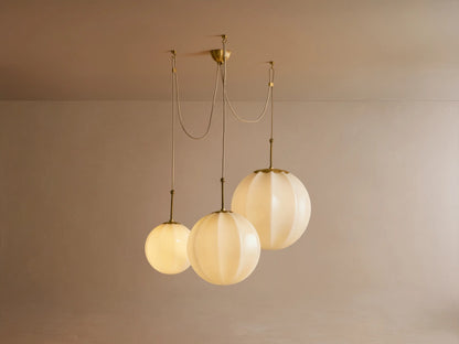 Close-up of Agnes Chandelier: Cream paneled glass globes glow softly, suspended by antique brass rods with knotted detail.