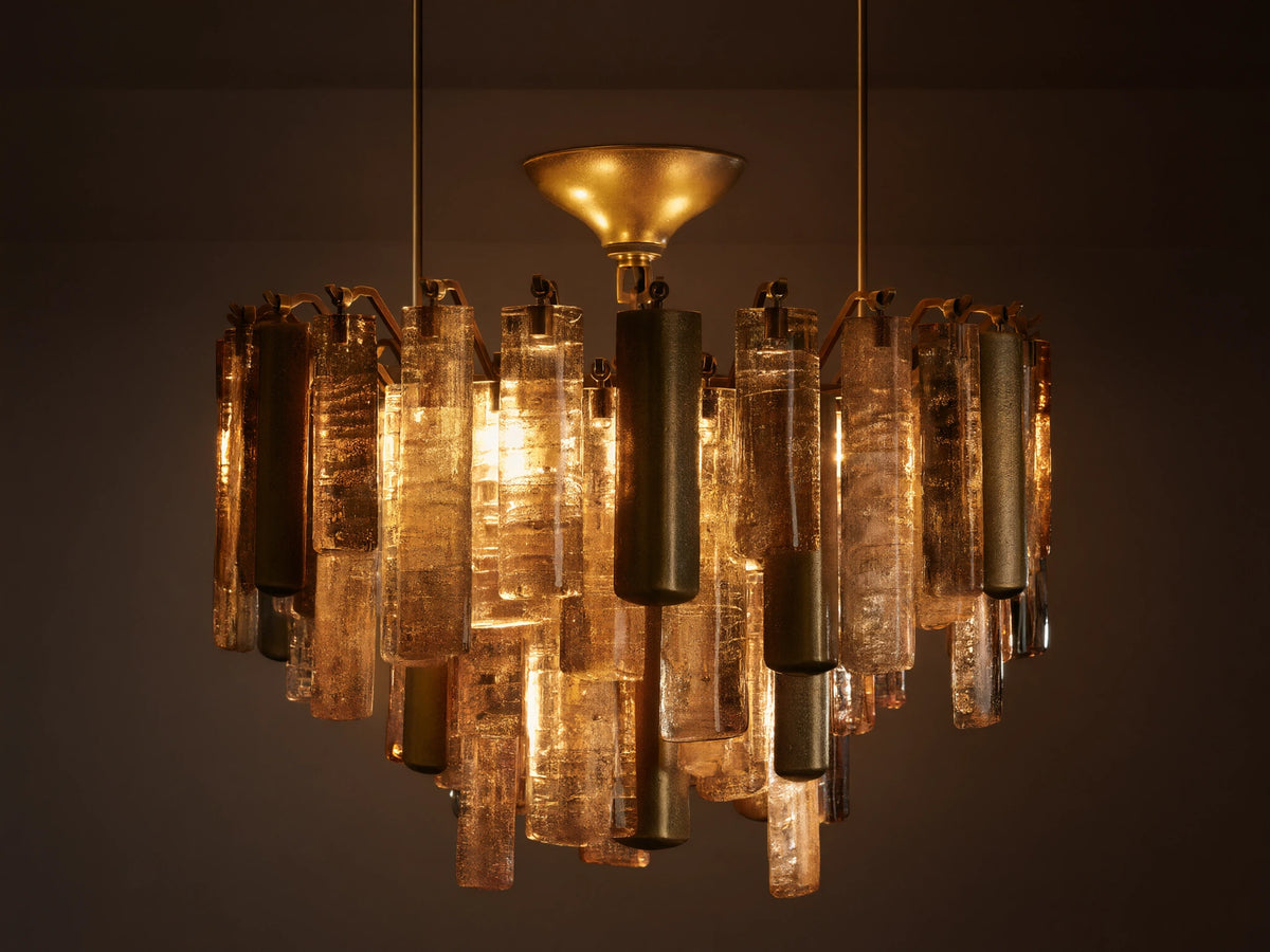 Neve Flush Mount, a round ceiling light with textured bronze cast glass rods & brass-finished aluminum cylinders, lit with a warm glow.