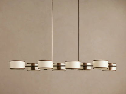 Daphne Fabric Linear Chandelier. Bronze frame, 6 white linen drum shades with black trim, hanging from ceiling.