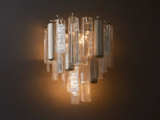 Neve Sconce: Wall-mounted light with clear textured glass and champagne-finished aluminum elements, glowing warmly.