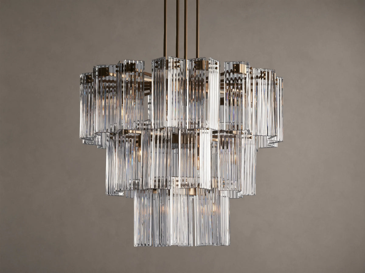 Delsie Round Chandelier, multi-tiered with clear ribbed glass rods and burnished brass frame, hanging against a brown wall.