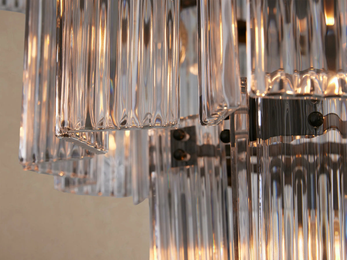 Delsie Round Chandelier: multi-tiered, clear fluted glass rods, dark metal frame, hanging against a light tan wall.