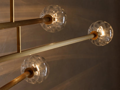 Close-up of an illuminated Brass and Glass Globe Chandelier‚Ñ¢ with clear, textured glass orbs and ribbed gold-toned arms.