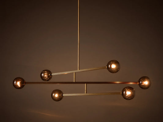 Modern chandelier with a vertical brass rod, horizontal ribbed brass arms, and six illuminated spherical smoky glass bulbs.