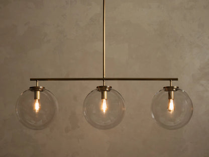 Front view of a brass chandelier with three clear glass globe shades, each containing an illuminated filament bulb.