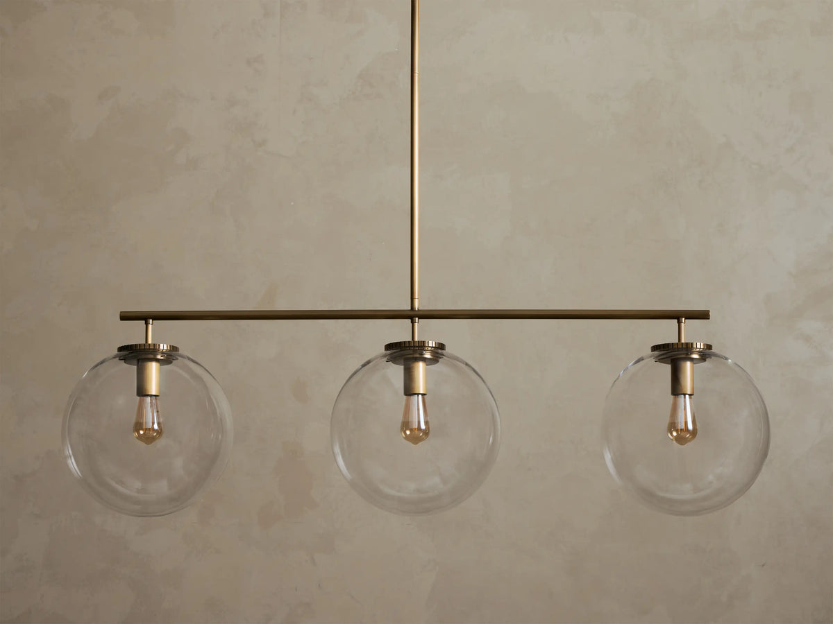 Front view of a brass chandelier with three clear glass globe shades, each containing an illuminated filament bulb.