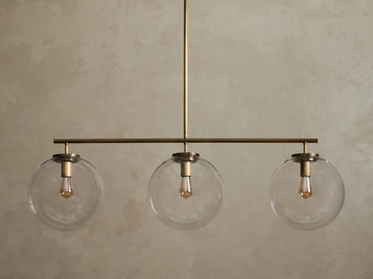Front view of a brass chandelier with three clear glass globe shades, each containing an illuminated filament bulb.