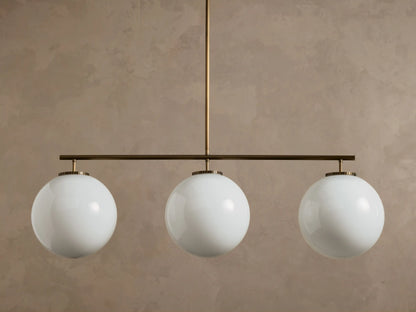Front view of a multi-globe pendant light with three white spherical glass globes on a bronze bar.
