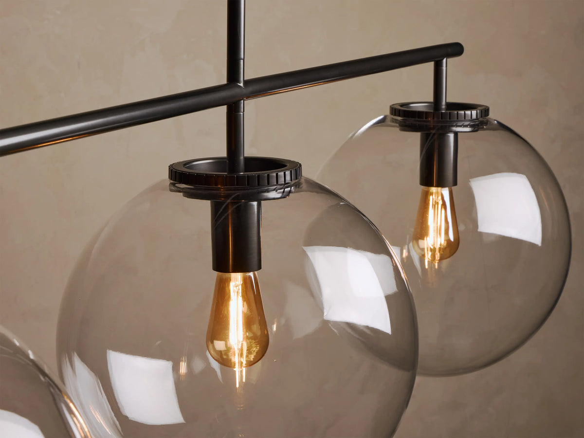 Close-up of a light fixture featuring a black metal frame, two smoky gray spherical glass shades, and warm glowing Edison bulbs.