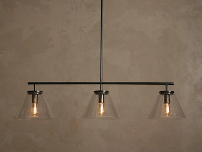 Front view of a black linear pendant light fixture with three clear conical glass shades and exposed warm Edison bulbs.