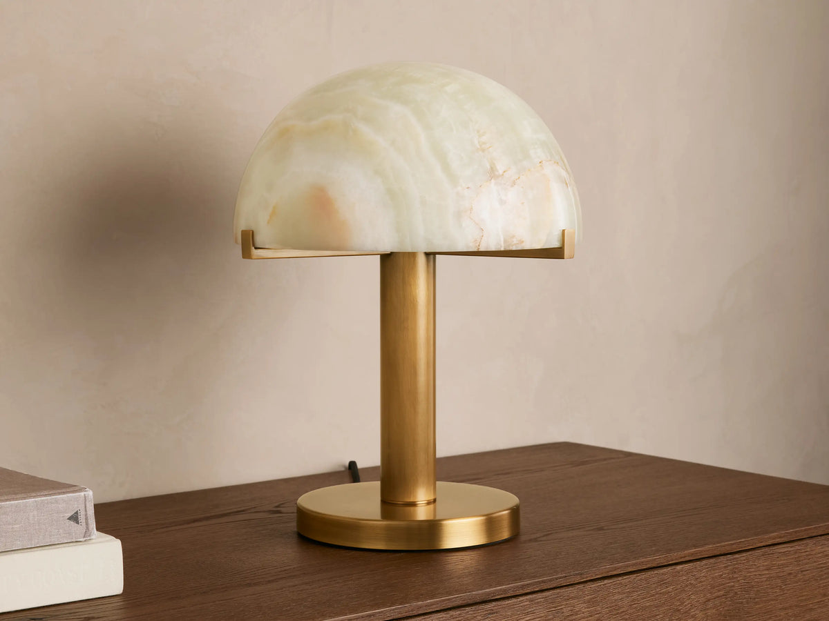 Emerie Table Lamp with a dome-shaped green onyx shade on a brass base, placed on a wooden surface against a neutral wall.