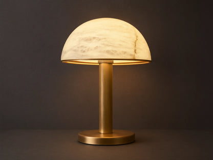 Emerie Table Lamp with alabaster stone shade and brass base on a wooden table, softly lit. Black fabric cord visible.