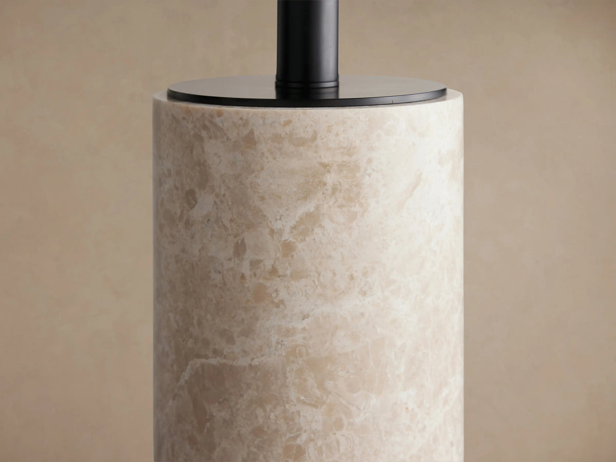 Brixton Table Lamp with a cylindrical creamy marble base, black stem, and round black fabric shade, on a wooden table.