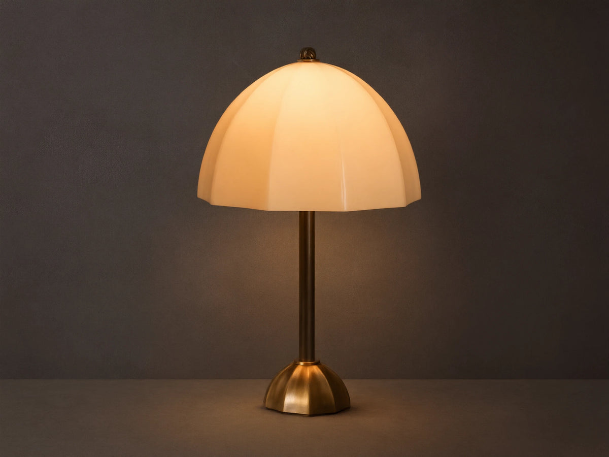 Front view of a cream ribbed glass table lamp with a brass stem and base, casting a warm glow on a wooden surface.