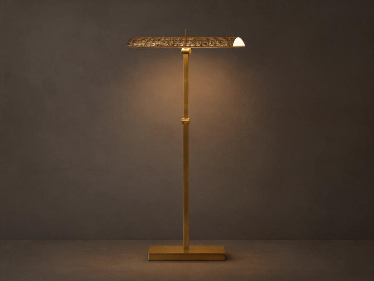 Abel Metal Floor Lamp: Upright, brass finish, rectangular base, long perforated shade emitting warm LED light. Beige wall, wood floor.