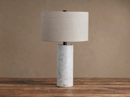 Brixton Table Lamp with cylindrical white marble base, black metal stem, and light beige fabric drum shade on a wooden table.
