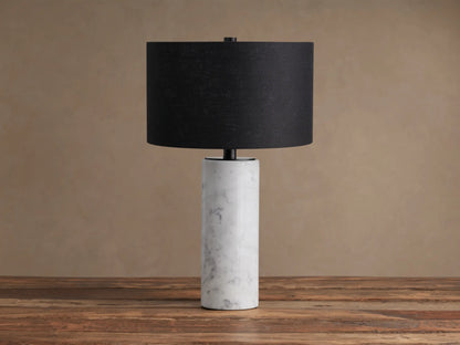 Brixton Table Lamp with a white cylindrical marble base and a black fabric drum shade, resting on a rustic wooden table.