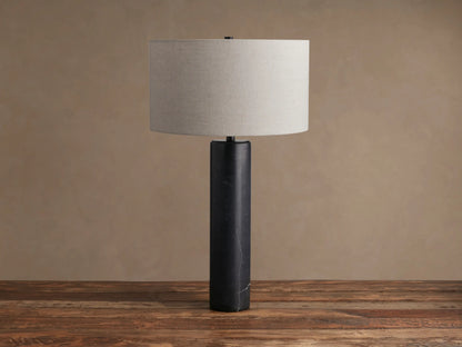 Brixton Table Lamp with a black marble cylindrical base and a light gray fabric drum shade, standing on a wooden surface.