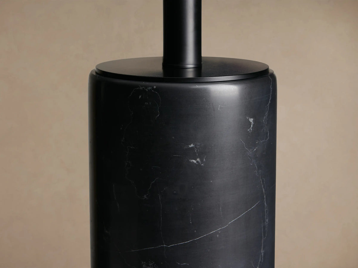 Brixton Table Lamp with a white cylindrical shade atop a black cylindrical marble base featuring natural veining, on a wooden table.