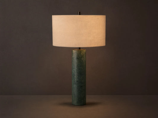 Brixton Table Lamp with a cylindrical green marble base and a large cream fabric lampshade, placed on a wooden surface against a gray wall.