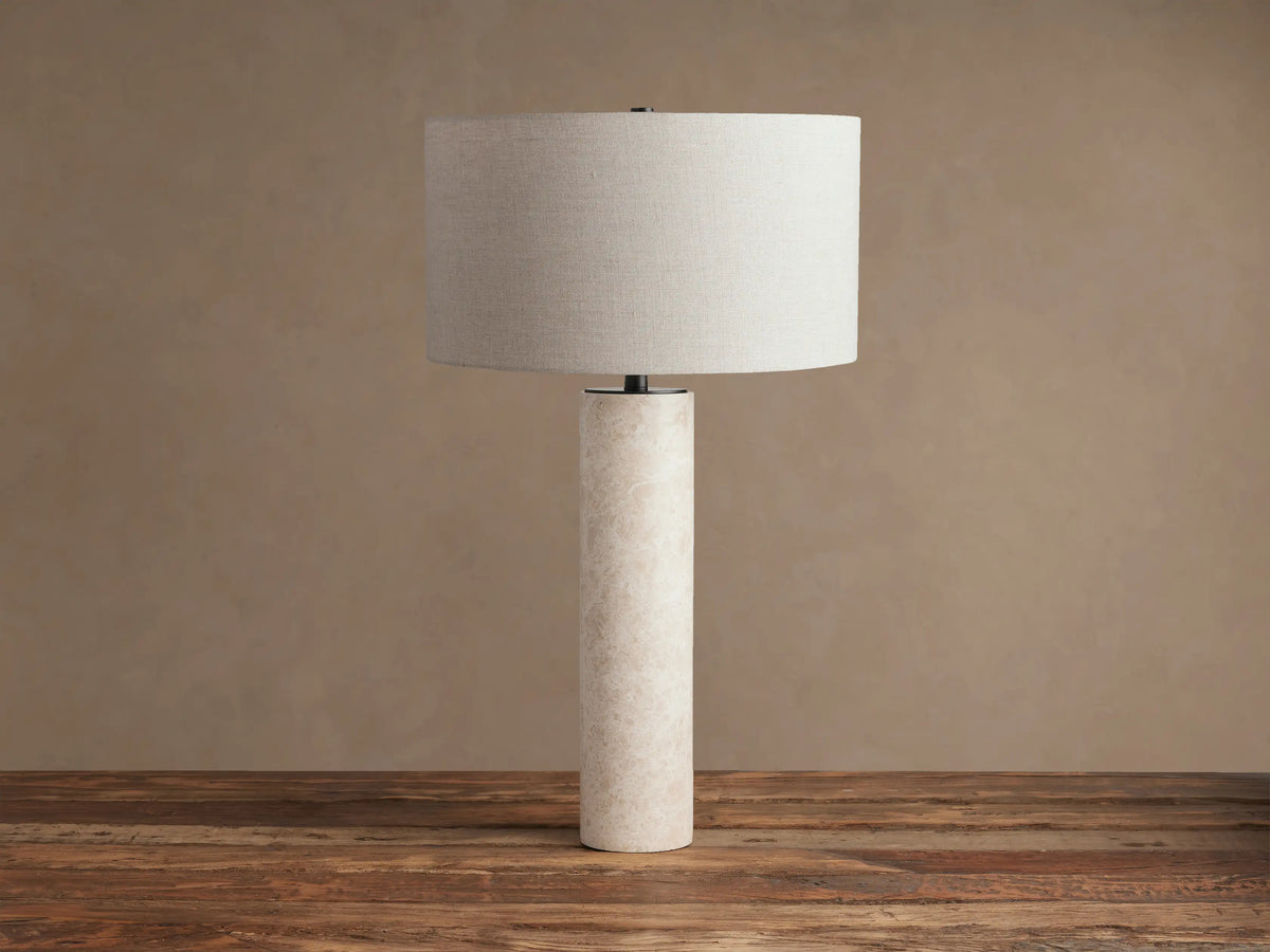 Brixton Table Lamp with a light marble cylindrical base and an off-white fabric drum shade on a wooden table.