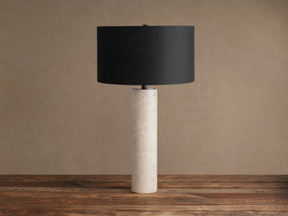 Brixton Table Lamp with a black cylindrical shade and a tall, cream-colored marble base, standing on a wooden table.