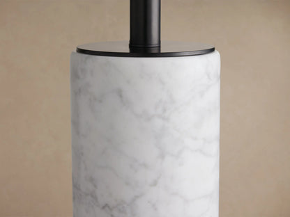 Brixton Table Lamp: white marble cylindrical base, black drum shade, on a wooden table against a brown wall.