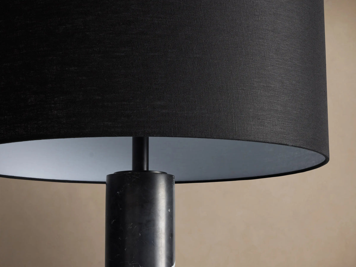 Brixton Floor Lamp with a black fabric drum shade and a tall, dark marble column, standing on a wooden floor.