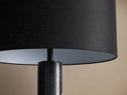 Brixton Floor Lamp with a black fabric drum shade and a tall, dark marble column, standing on a wooden floor.